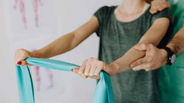 Woman stretching a resistance band while a therapist guides her arm