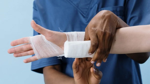 Person in blue scrubs bandaging a patient's wrist and hand