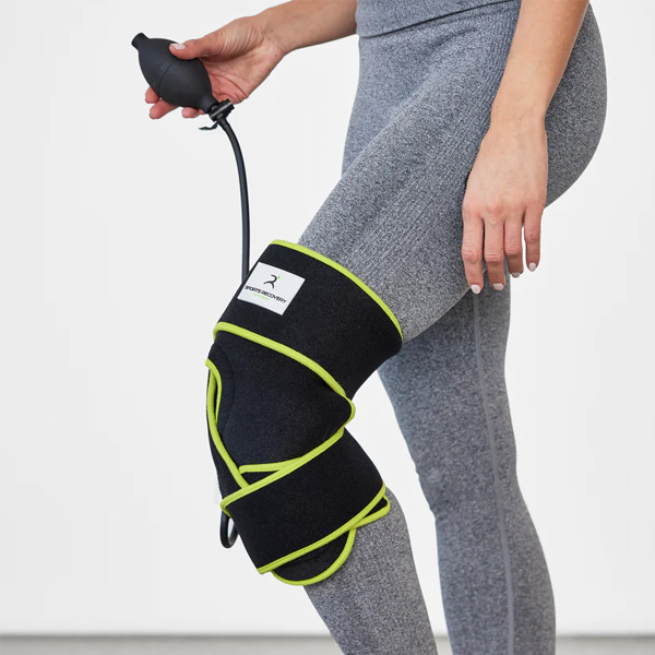 Black and yellow compression wrap on a woman's knee, connected to a hand pump